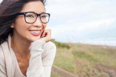woman with glasses smiling outside by the water