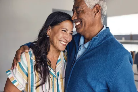 Two senior adults embracing each other with smiles.