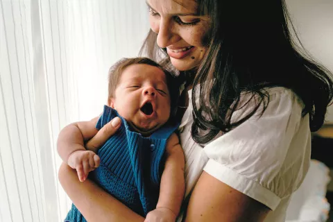 a smiling adult holding a yawning baby at home