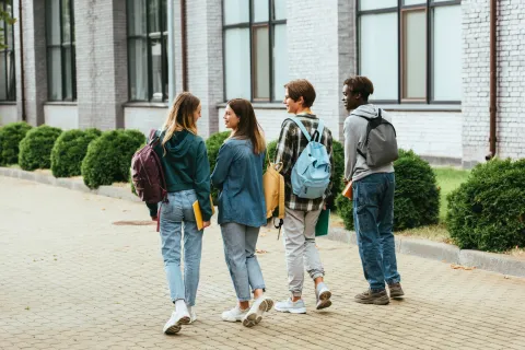 four students walking outside on a college campus wearing backpacks