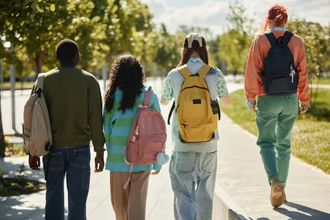 Four students walking side by side outside, facing away from the camera