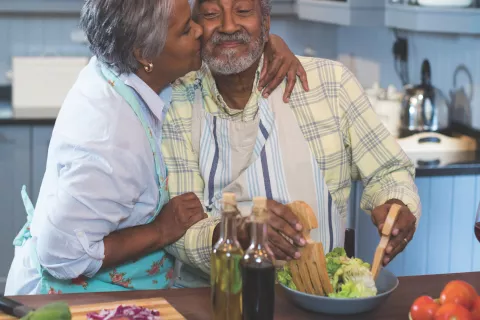 A woman kisses a man in the kitchen.