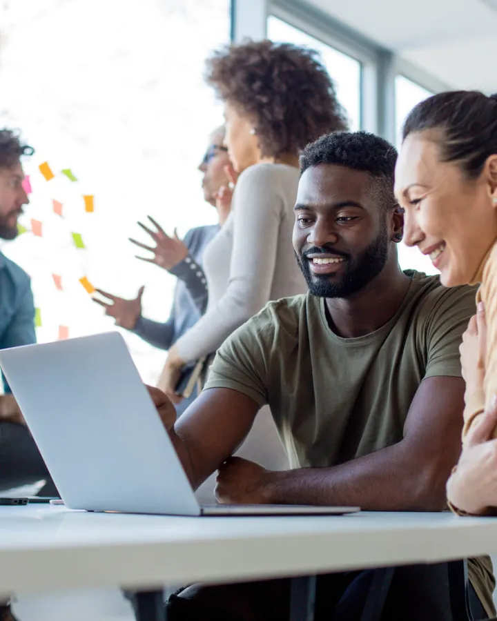 Two adults looking at a laptop while sitting at a desk in the office.
