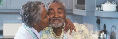 A woman kisses a man in the kitchen.